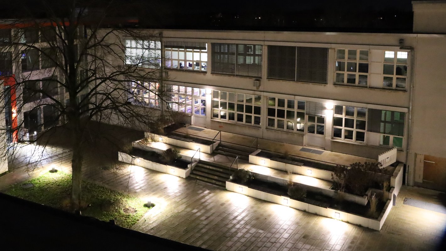 Gebäudeensemble der HBK bei Nacht, ein Innenhof mit Gebäude und teils beleuchteten Fenstern.