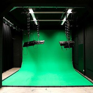 Ansicht auf ein Filmstudio. Ein Greenscreen wird von Deckenlampen ausgeleuchtet.