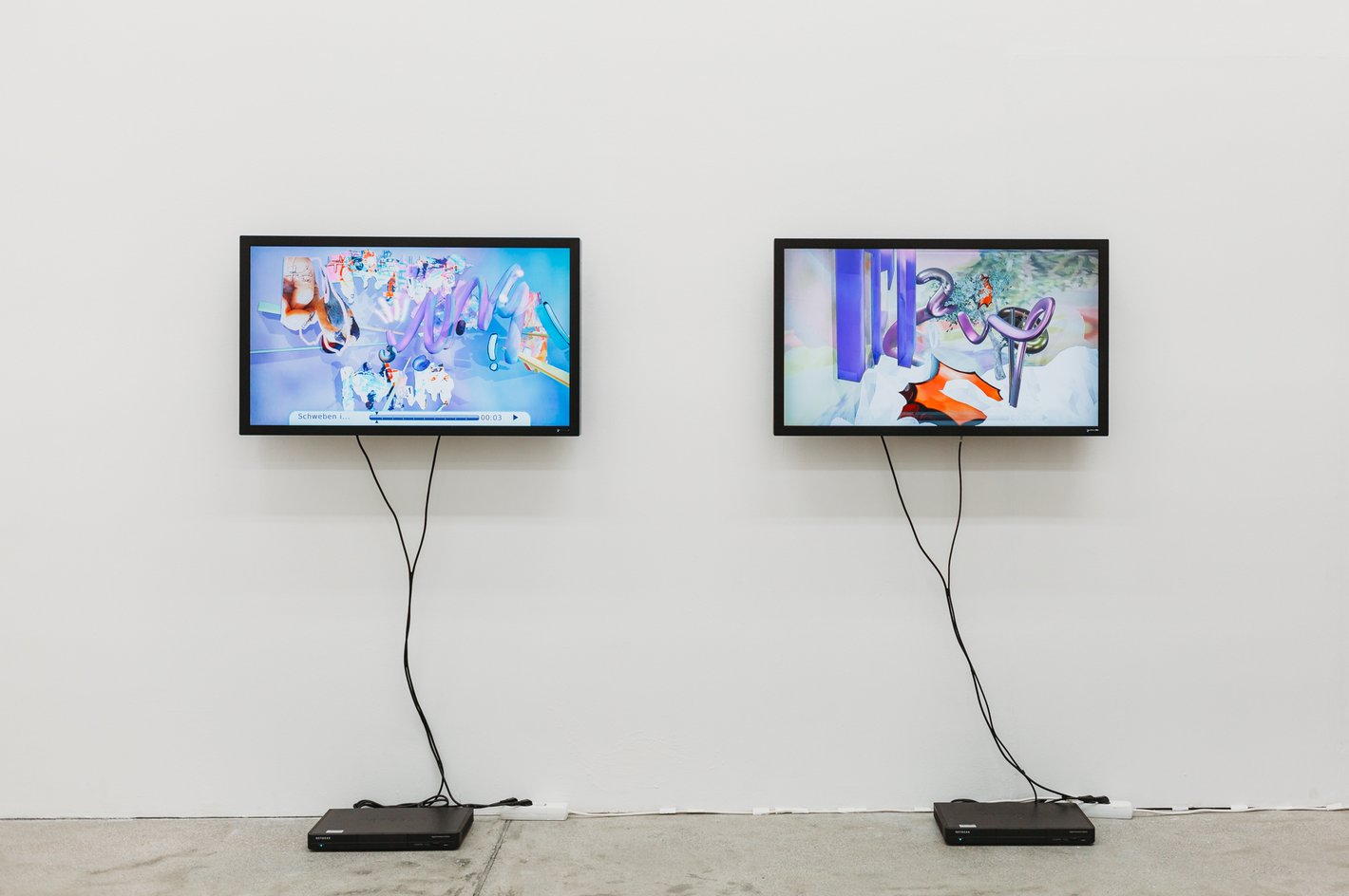 Ausstellungsansicht von zwei Monitoren die an einer Wand angebracht sind. Zu sehen sind zwei Animationen mit abstrakten Formen.